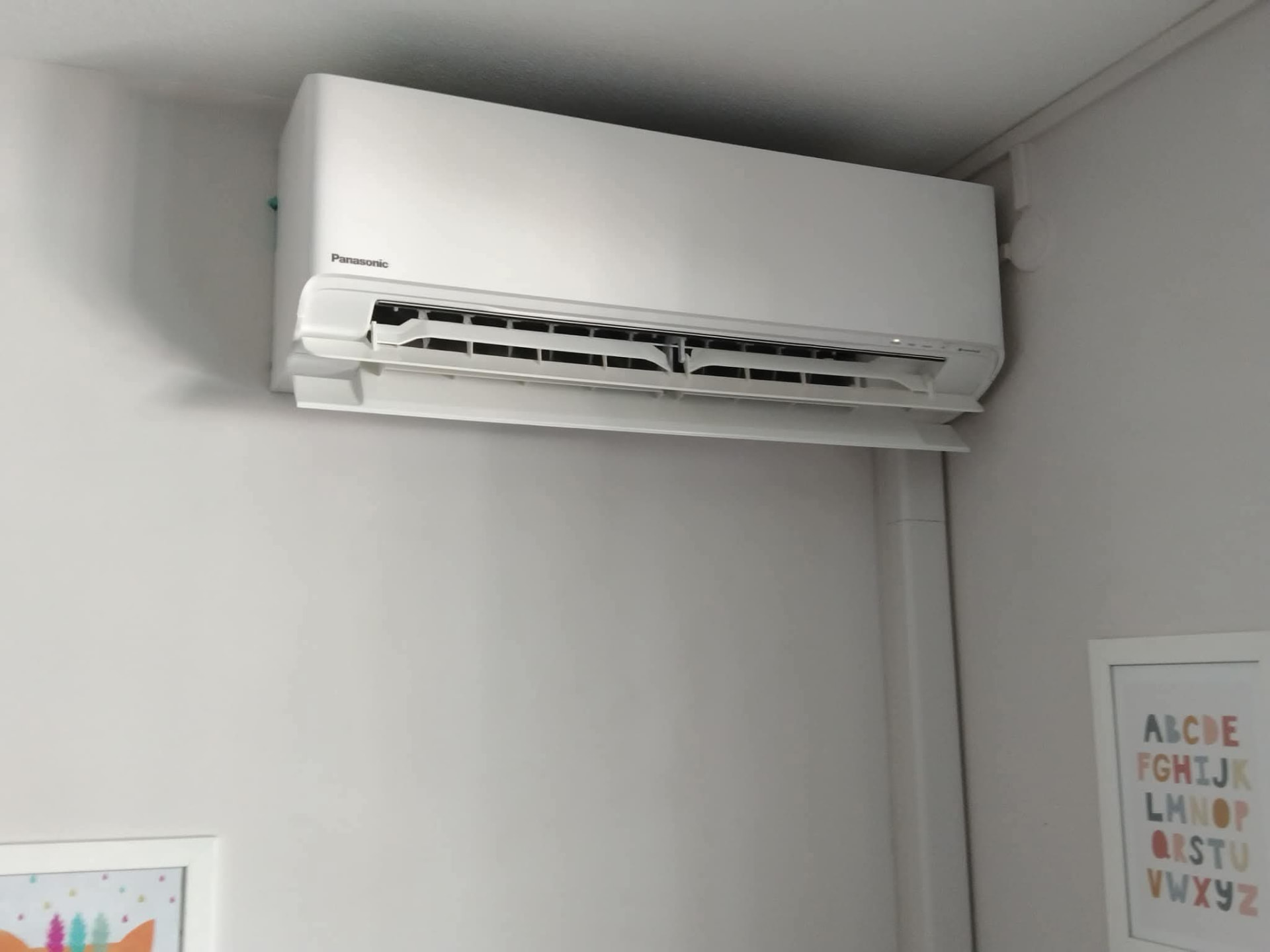 Remplacement 9K BTU Panasonic – Rivière Salée – climatisation Martinique Remplacement d'un climatiseur Panasonic 9 000 BTU à Rivière-Salée : unité murale installée en hauteur dans une chambre, au-dessus de cadres décoratifs – Rivière Salée, Martinique – LD CLIM 972