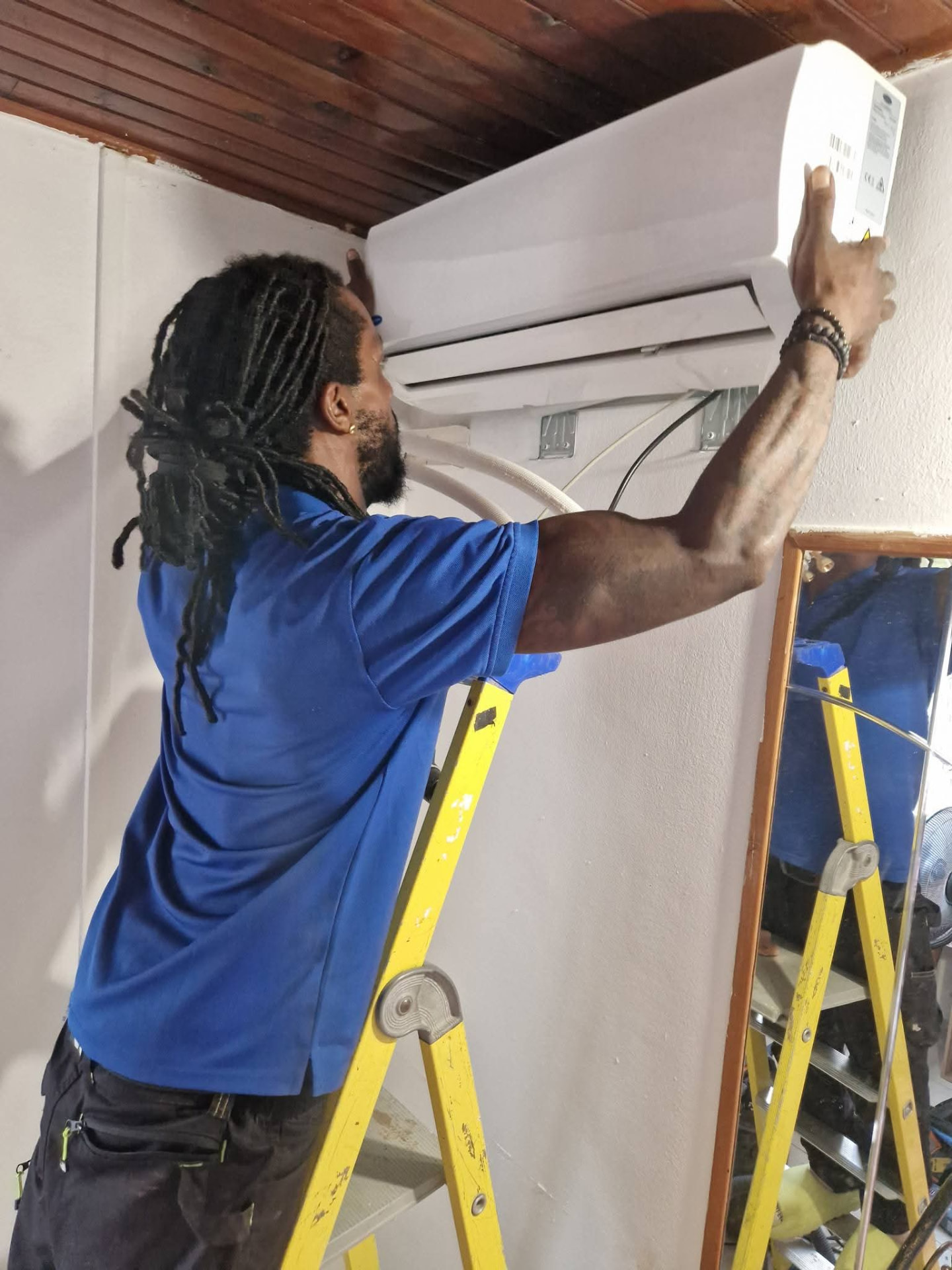 Laurent Despagne, fondateur et technicien de LD CLIM 972, posant une unité intérieure de climatisation murale sur une échelle chez un client en Martinique