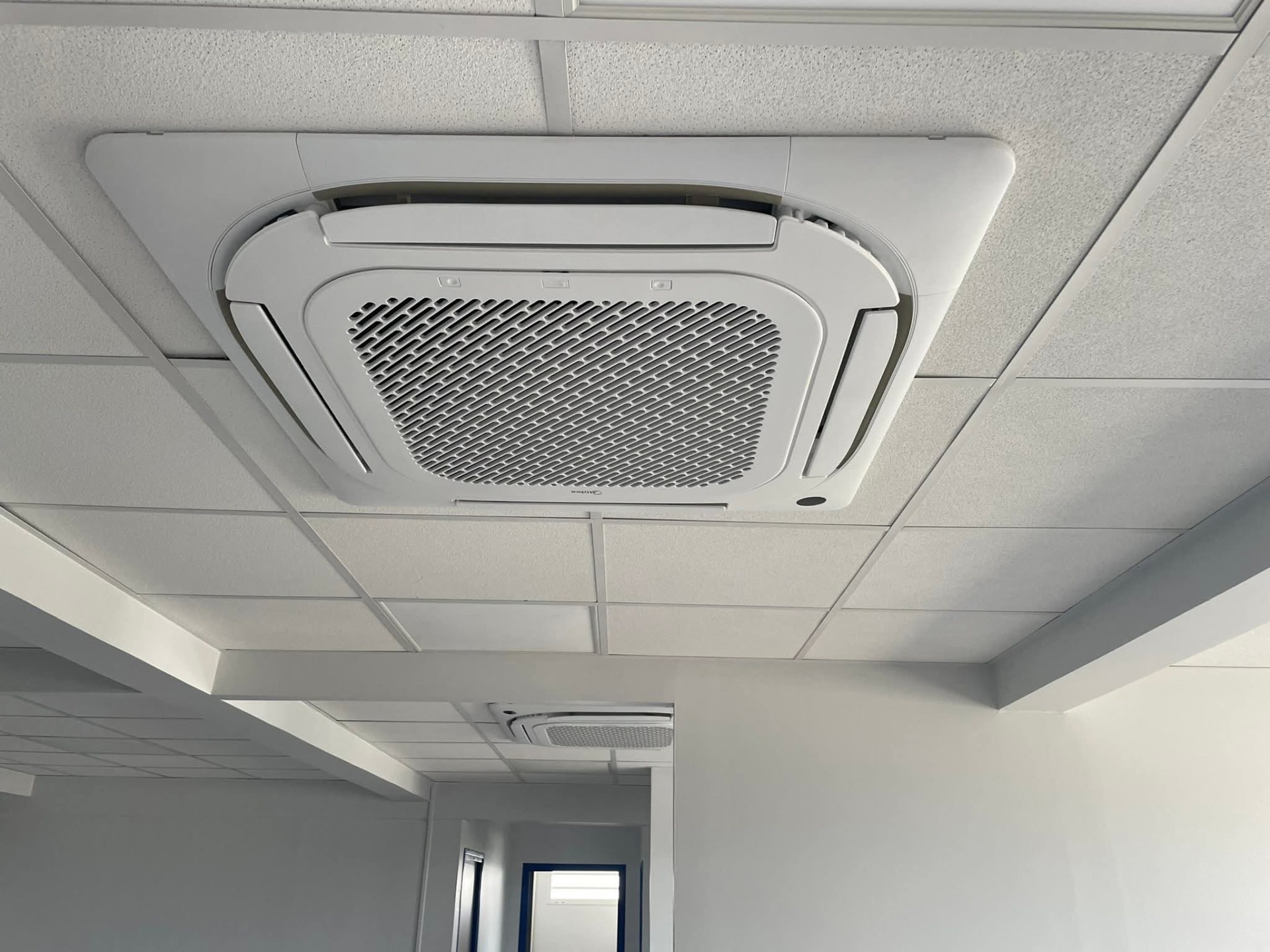Cassette de plafond Midea encastrée dans un faux-plafond blanc au Lamentin, une seconde cassette visible au fond du couloir pour climatiser tout l'étage – Lamentin, Martinique – LD CLIM 972