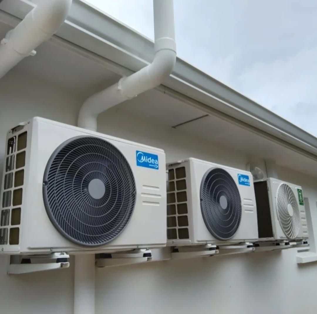 Unités extérieures Midea – climatisation Martinique Trois unités extérieures Midea fixées sur supports muraux sous un débord de toit, protégées de la pluie et du soleil, installation multi-appareils, Martinique – LD CLIM 972