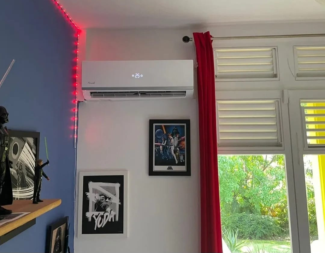 Unité intérieure murale Airwell – climatisation Martinique Unité intérieure murale Airwell posée par LD CLIM 972 dans une chambre, fixée en hauteur au-dessus de cadres décoratifs pour une diffusion homogène de l'air frais, Martinique – LD CLIM 972