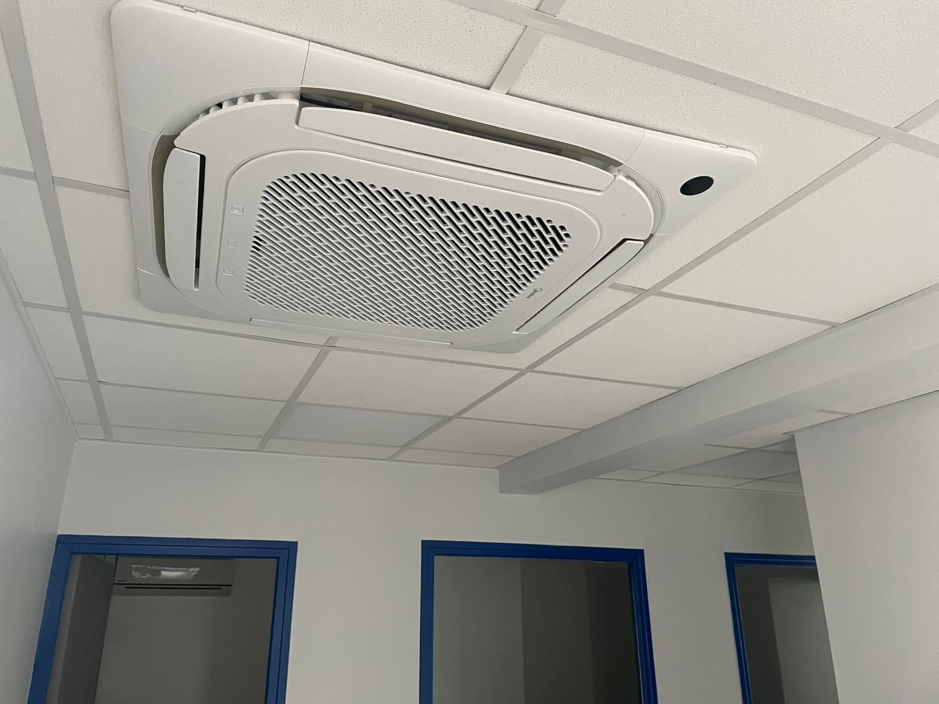 Installation – Lamentin – climatisation Martinique Installation au Lamentin : cassette de plafond Midea encastrée dans le faux-plafond d'un bureau, au-dessus de trois portes à encadrements bleus – Lamentin, Martinique – LD CLIM 972