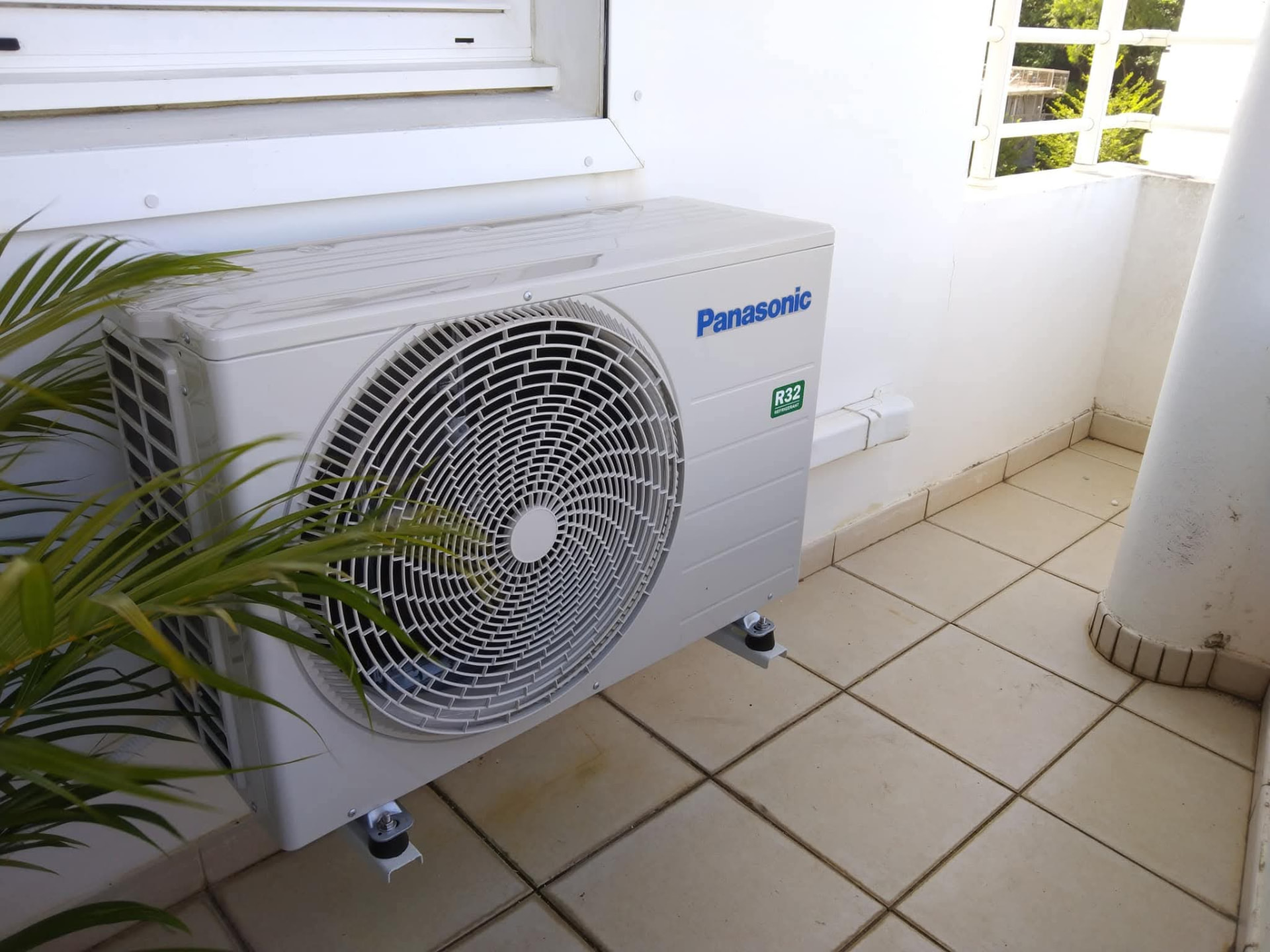 Remplacement 9K BTU Panasonic – Rivière Salée – climatisation Martinique Unité extérieure Panasonic 9 000 BTU posée sur consoles murales avec plots antivibratiles sur une terrasse carrelée à Rivière-Salée, pour limiter bruit et vibrations – Rivière Salée, Martinique – LD CLIM 972