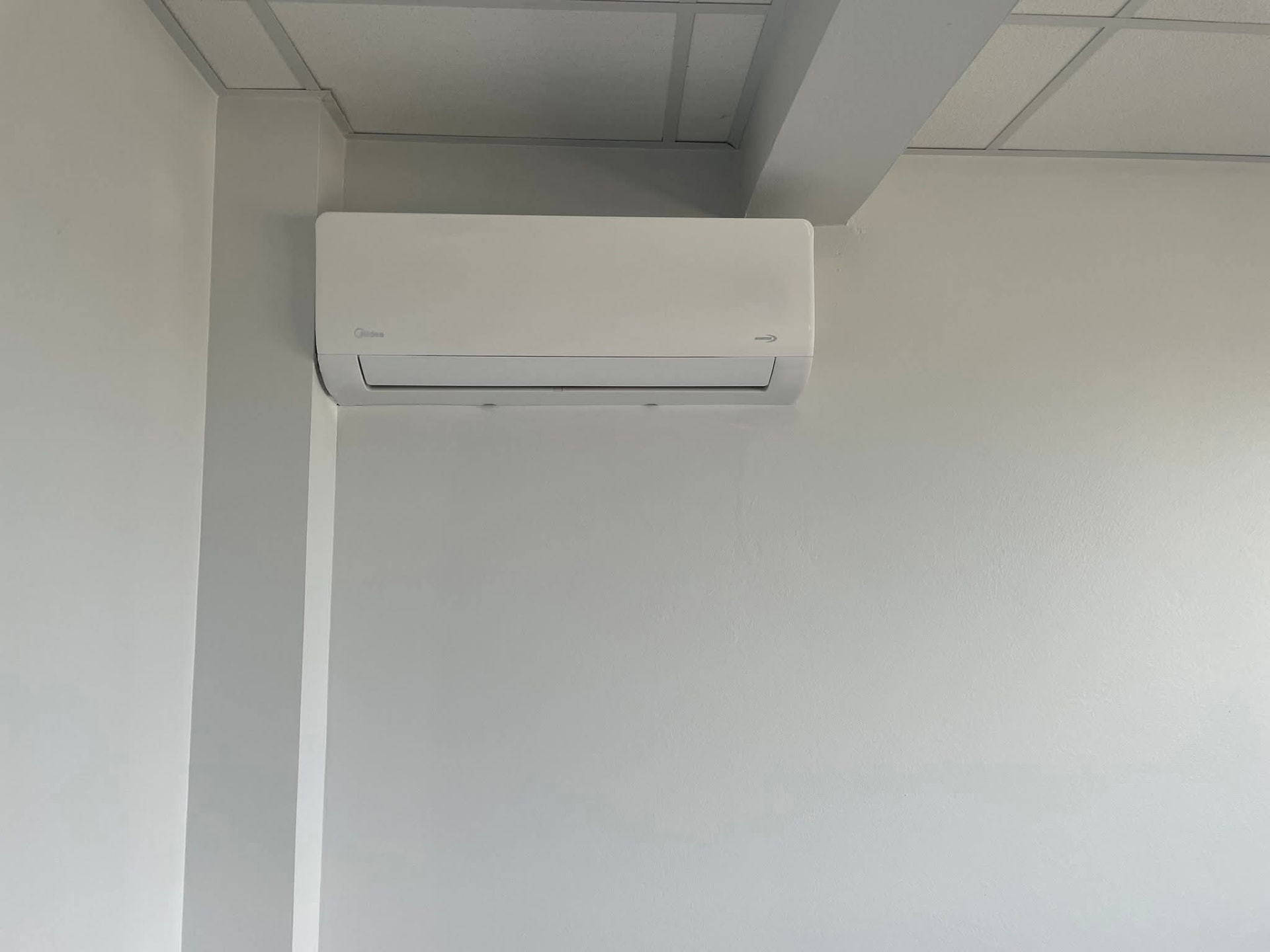 Climatiseur mural Midea fixé en partie haute d'un mur blanc au Lamentin, aligné le long d'un décroché de mur sous le plafond pour une pose discrète – Lamentin, Martinique – LD CLIM 972